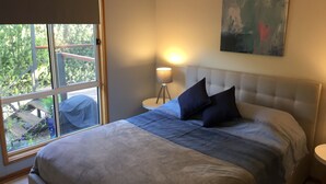 A bedroom with a bed, a bedside lamp, a painting, and a view through a window.