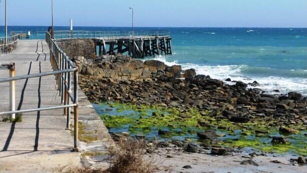 A pier extending into the sea with a rocky shoreline and a clear sky.