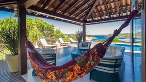 Un hamac sur une terrasse couverte donnant sur une piscine et l’océan.