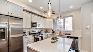A modern kitchen with stainless steel appliances, white cabinetry, and pendant lighting.