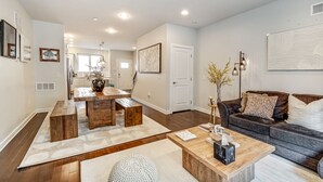 A modern living room with a wooden coffee table, a dark sofa, and a dining area with a wooden table and benches.