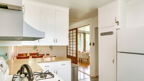 Una cocina con armarios blancos, una estufa a gas y un refrigerador. Hay una mesa de comedor con sillas y se ve una habitación tradicional japonesa al fondo.
