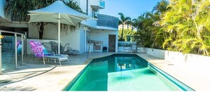 Relax by the pool surrounded by palm trees and a covered patio with lounge chairs.