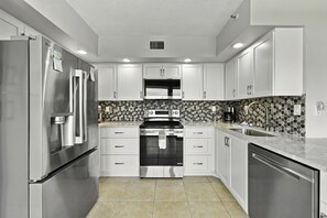 A modern kitchen with stainless steel appliances, white cabinetry, a microwave, and a patterned backsplash. - Bay Front Serenity: 4th Floor 2BD/2BA at Isla Del (Isla Del Sol)