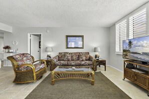 A living room with a sofa, two armchairs, a coffee table, a television, and a framed picture on the wall.