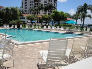 A pool area with lounge chairs and a building in the background. - Bay Front Serenity: 4th Floor 2BD/2BA at Isla Del (Isla Del Sol)