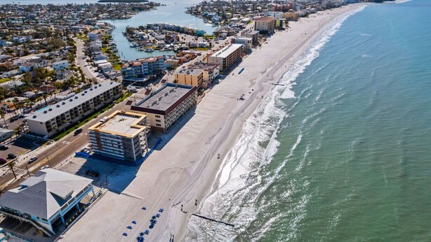 An aerial view of a coastal city with a long beach, a marina, and a mix of residential and commercial buildings.