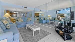 A modern living room with a sofa set, a coffee table, a TV, and a kitchen in the background.
