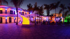 A hotel with a modern design, featuring a central staircase, outdoor seating area, and palm trees.