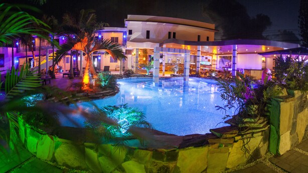 A nighttime resort with a swimming pool, palm trees, and a building with illuminated windows.
