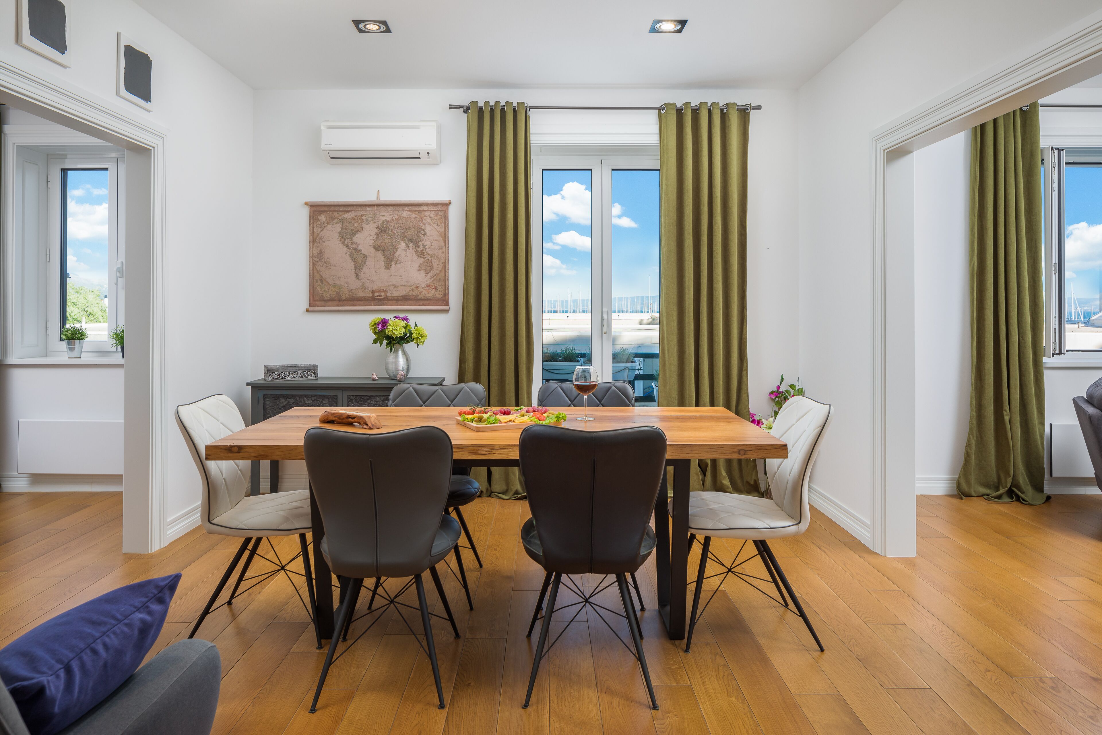 A dining area with a wooden table, four chairs, a vase with flowers, and a view of the sea through large windows.