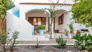 Un bâtiment blanc avec un escalier bleu, une porte en bois et un petit porche agrémenté de plantes en pot et d’un barbecue.