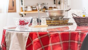 Une cuisine avec une nappe à carreaux rouges, un saladier en verre rempli de baies rouges, deux salières et poivrières, une casserole en métal posée sur un plateau en osier, et un panier en osier contenant un bocal en verre.