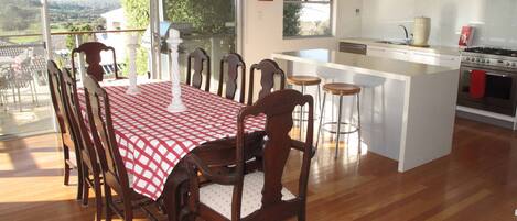Un coin repas avec une table et des chaises, une cuisine équipée d’une cuisinière et d’un évier, et de grandes fenêtres offrant une vue dégagée.