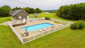 A rectangular swimming pool with a white deck, surrounded by a white fence. There are lounge chairs and a small table near the pool.