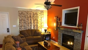 A living room with a sofa, coffee table, fireplace, and a television mounted above the fireplace.