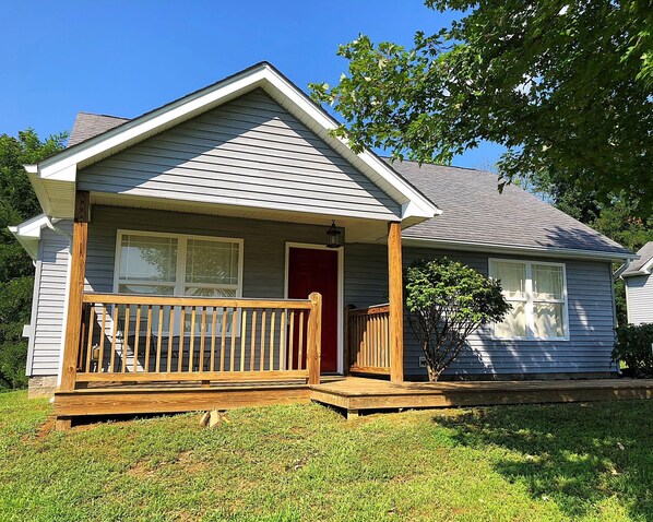 A single-story house with a front porch, a red door, and a small front yard.