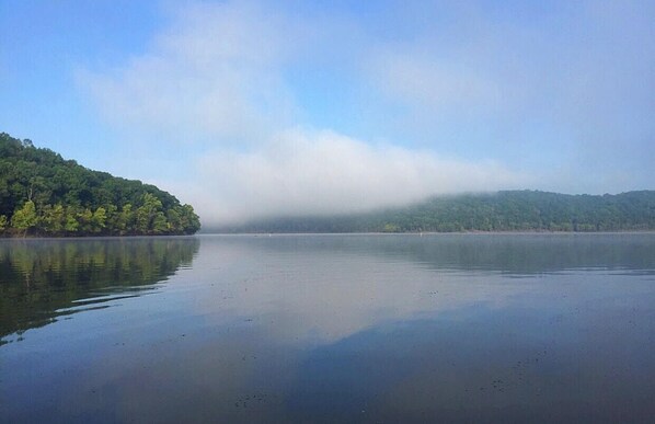Un lago tranquilo con una isla boscosa y una colina brumosa en la distancia.