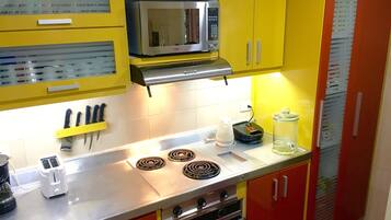 A kitchen with yellow cabinets, a microwave, a stove, a toaster, and a kettle.