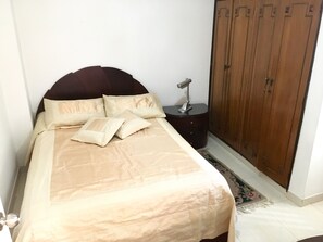 Een slaapkamer met een bed, kussens, een nachtkastje en een kledingkast.