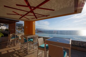 A terrace with wicker chairs and a glass table, overlooking a coastal view.