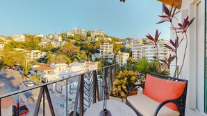 A balcony with a wicker chair and potted plants, overlooking a residential area with various buildings and a clear sky. - Charming Condo in V177! 1BD Condo for rent in Old Town, Puerto vallarta (Puerto Vallarta)