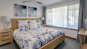A modern bedroom with a wooden bed, two wall-mounted paintings, a ceiling fan, and a large window with curtains. - Seas the Day - Lakefront getaway by the beach (Encounter Bay)