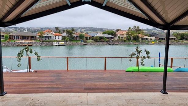 A covered deck with a view of a calm lake, houses in the background, and a stone wall. - Seas the Day - Lakefront getaway by the beach (Encounter Bay)