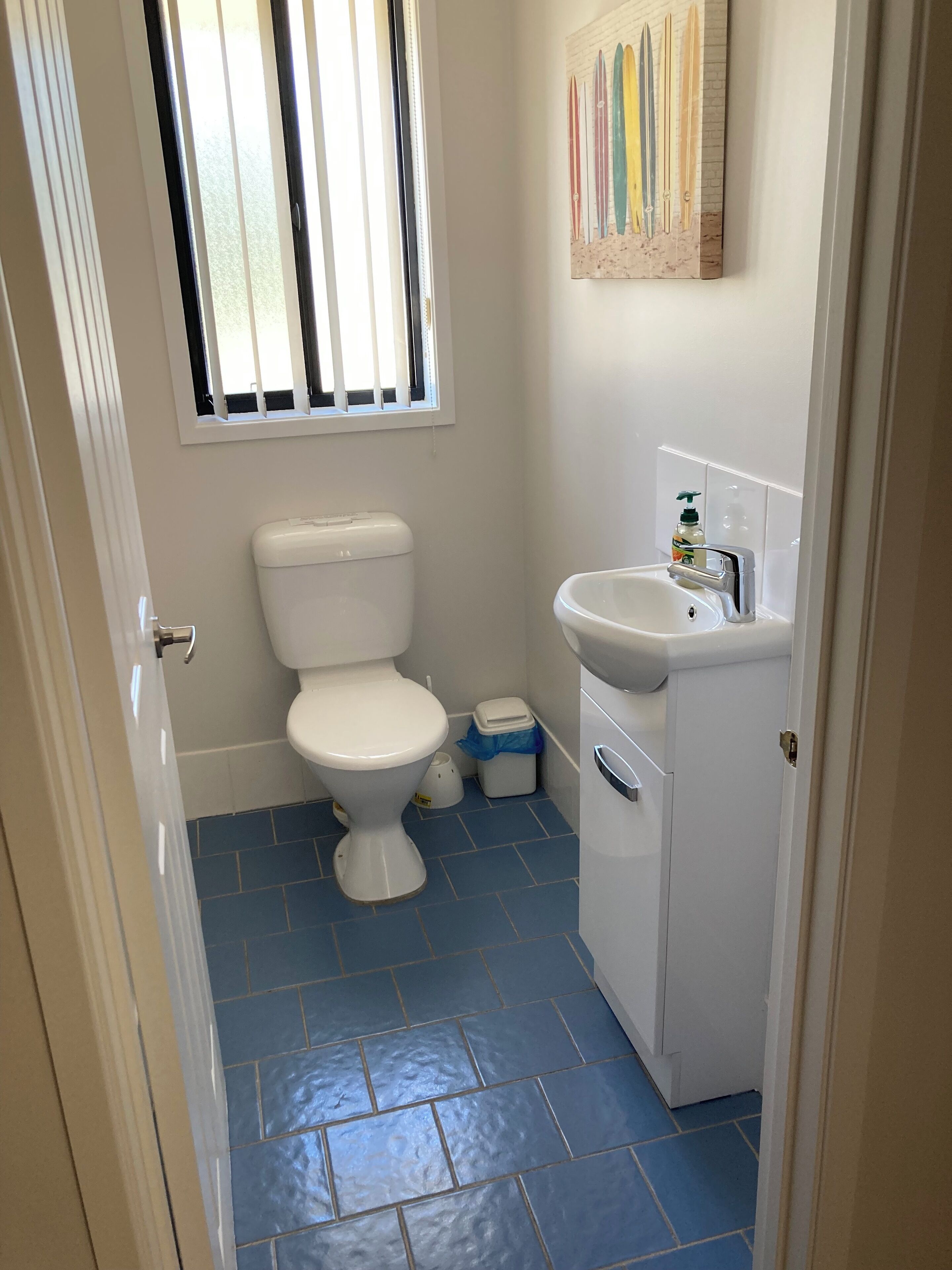 A small bathroom with a toilet, sink, and a window with blinds.