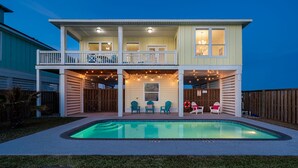 Una casa de dos pisos con balcón, piscina y mobiliario exterior.