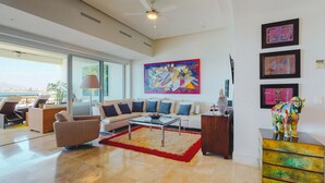 Un salon spacieux avec une grande fenêtre, un canapé, une table basse et un tableau abstrait aux couleurs vives.
