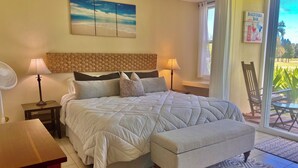 Une chambre avec un grand lit, des lampes de chevet, une tête de lit en bois, une petite table et une vue sur l’extérieur grâce à une porte-fenêtre coulissante.