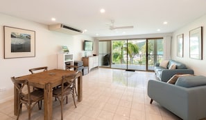 A modern living room with a dining area, large windows, and a sliding glass door leading to an outdoor area. - Le Jarden Vue Du Port - Airlie  Beach (Airlie Beach)