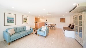 A spacious living area with a sofa, armchair, and a dining table. - Le Jarden Vue Du Port - Airlie  Beach (Airlie Beach)