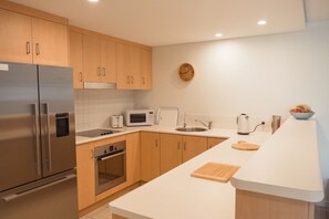 Cozinha moderna com eletrodomésticos de aço inoxidável, armários de madeira, micro-ondas e chaleira.