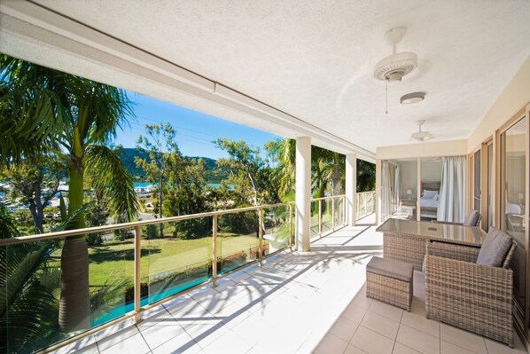 A balcony with a glass railing overlooking a swimming pool and lush greenery.