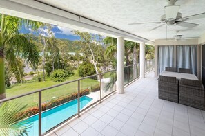 A balcony with a pool view, ceiling fans, and outdoor furniture. - Le Jarden Vue Du Port - Airlie  Beach (Airlie Beach)