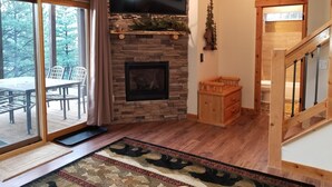A living room with a stone fireplace, a flat-screen TV mounted above it, and a wooden staircase leading to another level. -  RIDGEVIEW RETREAT/ Huge views! Hot tub, fireplaces, A/C,  and location! (Estes Park)