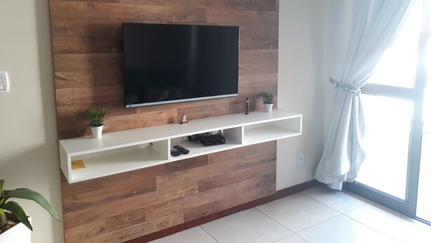 A modern living room with a wooden wall-mounted TV, white shelves, and a potted plant. - Fully furnished apartment with 3 bedrooms and 2 parking spaces. (Prainha)