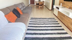 A modern living room with a sofa, a dining table, and a TV mounted on the wall. - Fully furnished apartment with 3 bedrooms and 2 parking spaces. (Prainha)