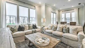 A spacious living room with two beige sofas, a wooden coffee table, and a large window with curtains.