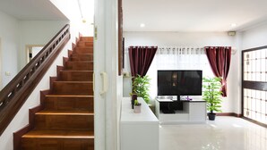 A modern living room with a wooden staircase, a flat-screen TV, and two potted plants. - Large 3 Bedroom House Near Old City and Night Bazaar  (Tambon Hai Ya)
