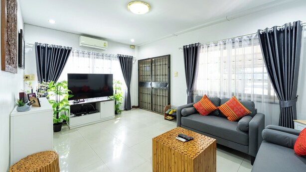 A modern living room with a flat-screen TV, grey sofa, wooden coffee table, and potted plants. - Large 3 Bedroom House Near Old City and Night Bazaar  (Tambon Hai Ya)
