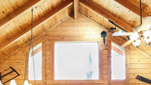 A cozy cabin interior with a wooden interior, a fireplace, a television mounted on the wall, and a large window providing natural light. -  Branson MO Log Cabin Private Porch Quiet Mtn. Forest View Above Lake, Handicap  (Blue Eye)