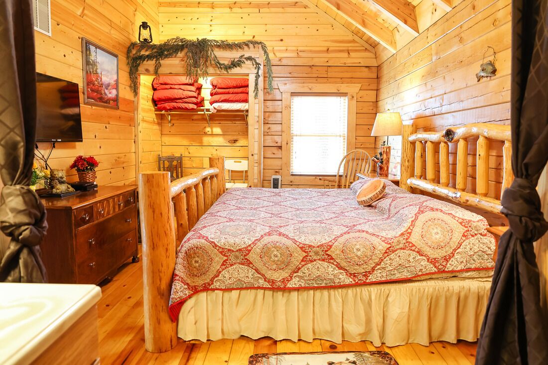 Camera da letto in un accogliente chalet in legno, con un letto, una cassettiera, un televisore e una finestra.