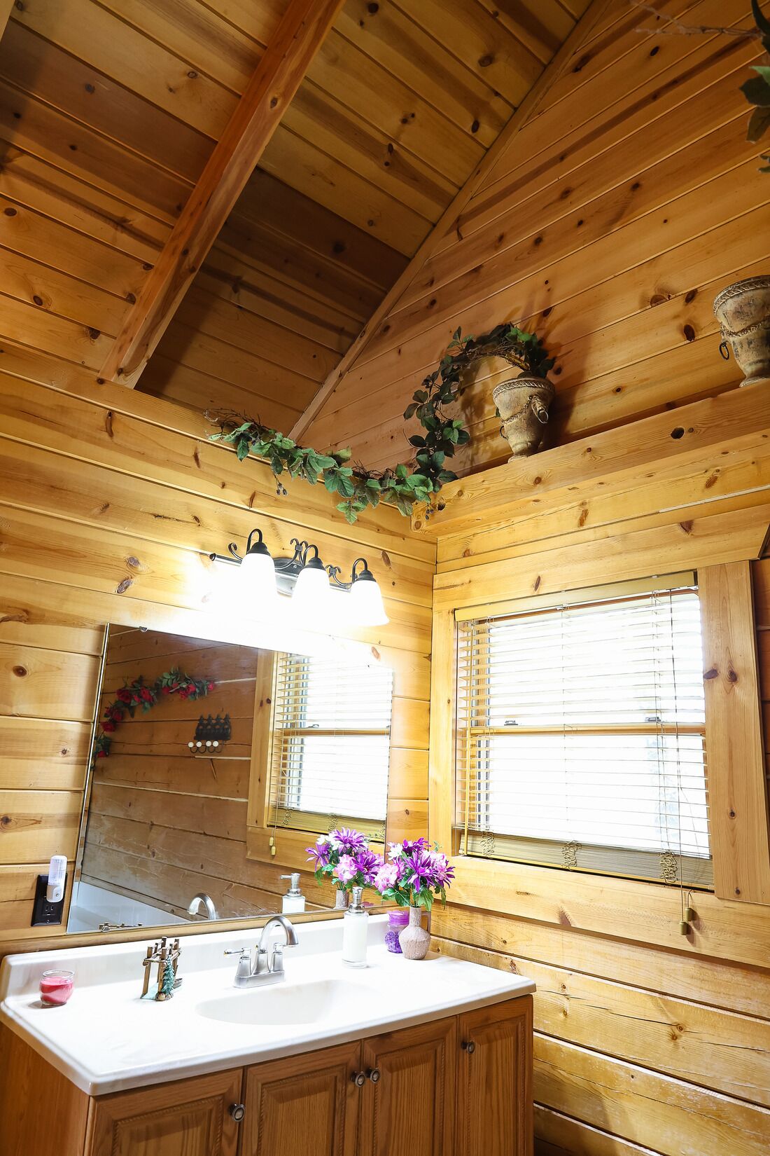 A wooden cabin bathroom with a sink, mirror, and window.