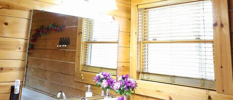A wooden cabin bathroom with a sink, mirror, and window.