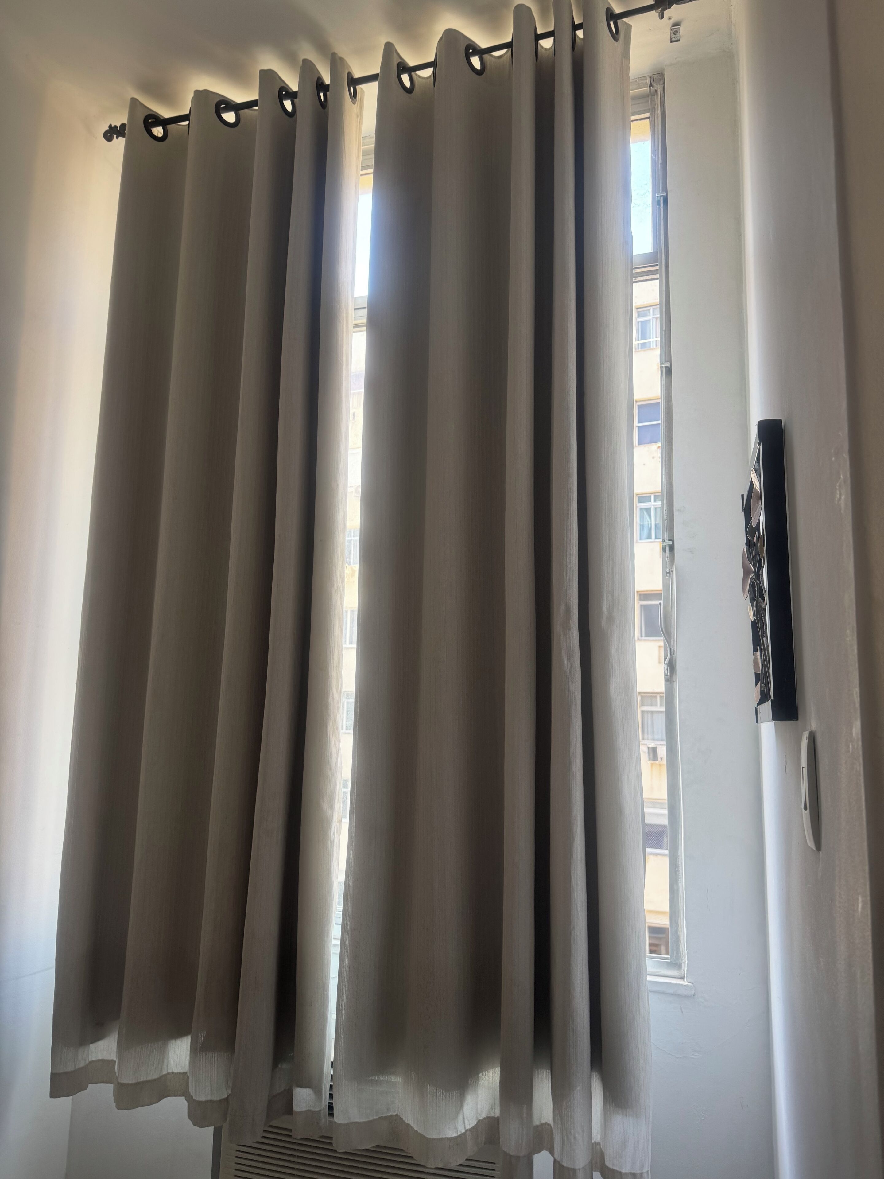 A window with a white curtain and a black security device on the wall.