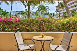 Un balcon agrémenté de deux chaises et d’une petite table, entouré d’une végétation luxuriante et de fleurs aux couleurs vives.