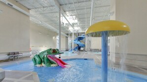 Een overdekt waterpark met een glijbaan in de vorm van een kikker en een waterfontein.